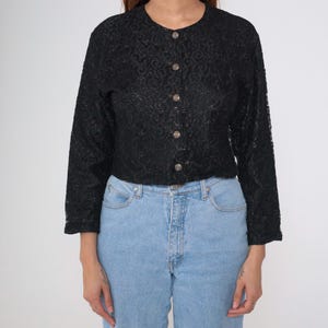 Puede incluir: Top de encaje negro con botones, mangas largas y cuello redondo. El top presenta un delicado estampado floral y se abrocha en la parte delantera con cinco botones redondos. Se combina con vaqueros de mezclilla azul claro.