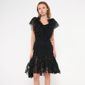 May include: A black lace dress with a ruffled neckline and short sleeves. The dress has a fitted bodice and a flared skirt, creating a classic silhouette. The dress is made of delicate lace fabric.