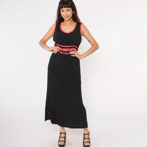 May include: A black maxi dress with red trim around the neckline and waist. The dress has a sleeveless design and a simple, flowy silhouette.