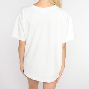 Puede incluir: Una camiseta blanca de gran tama&ntilde;o con mangas cortas.