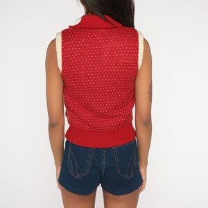 May include: Red sleeveless sweater vest with white trim and a mock neck. The vest has a small white polka dot pattern.