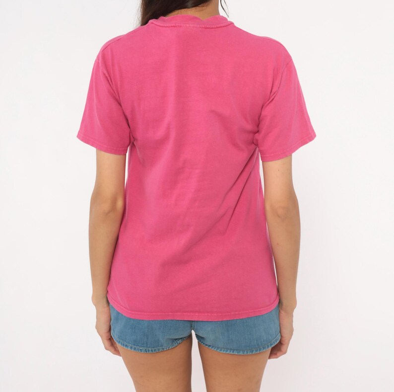 May include: A solid hot pink short-sleeved t-shirt with a crew neckline paired with blue denim shorts. The t-shirt features a plain back design with visible stitching along the sleeves and hemline, while the shorts have a classic five-pocket style.