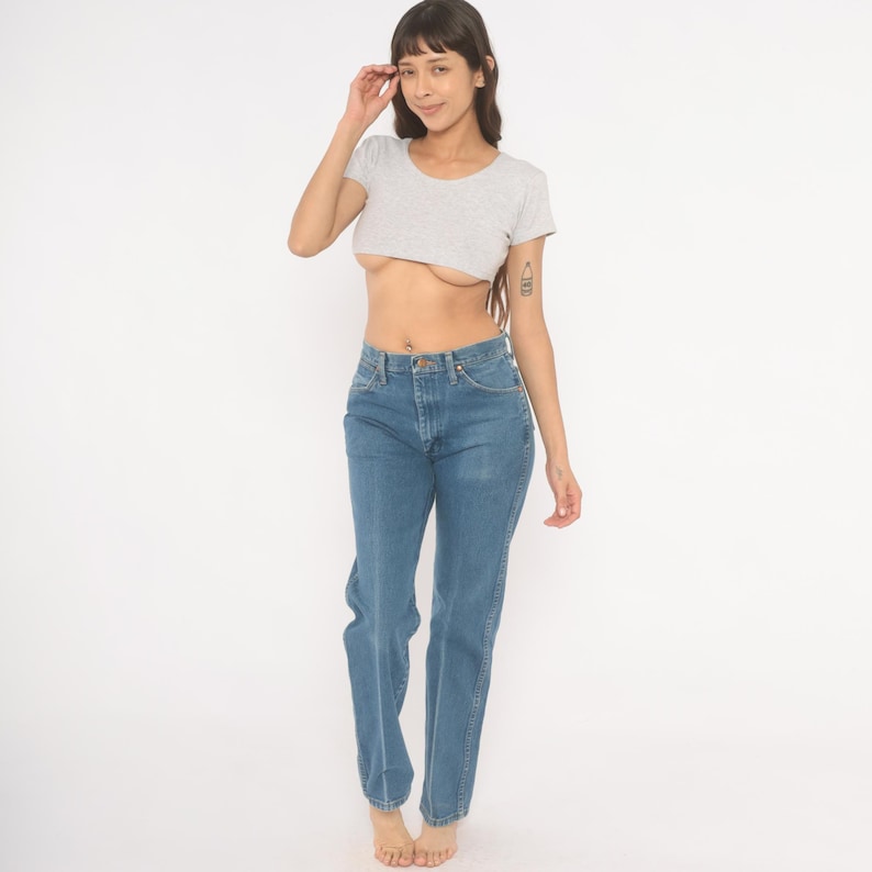 May include: A light gray crop top and blue jeans. The short-sleeved top has a round neckline. The jeans are a medium wash denim with a classic five-pocket design.