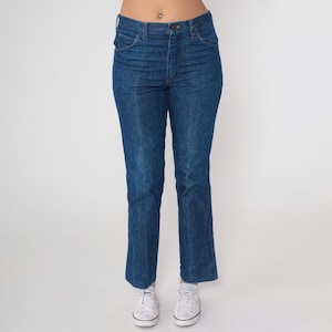 May include: Dark blue denim jeans with a classic straight leg fit. The jeans have a button and zipper closure, front and back pockets, and belt loops. The jeans are worn with white sneakers.