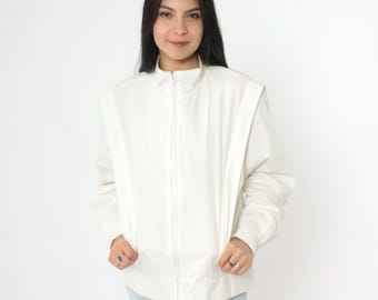 May include: A white zip-up jacket with a stand-up collar and long sleeves. The jacket has a slightly oversized fit and features a zipper closure.