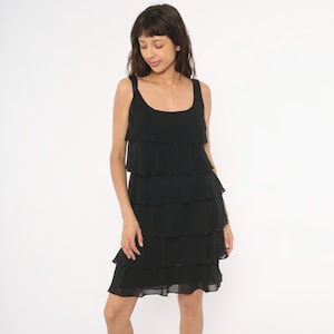 May include: A black sleeveless dress with a tiered, ruffled skirt. The dress has a scoop neckline and thin straps. The fabric appears to be a lightweight material, and the dress falls to about knee length.
