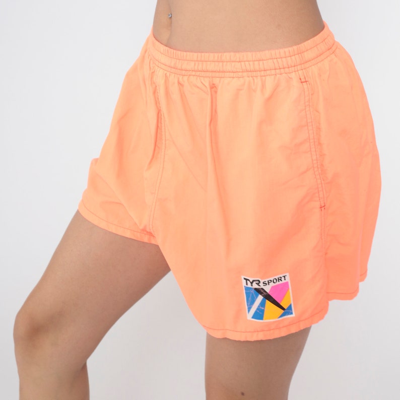 May include: Orange athletic shorts with a TYR SPORT logo in a colourful geometric design.