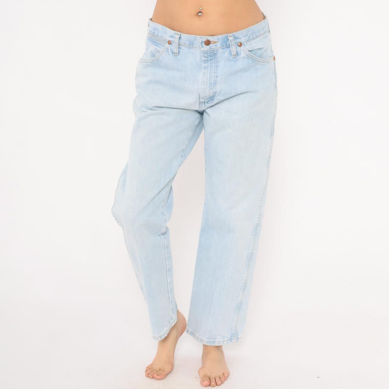 May include: Light blue denim jeans with a classic five-pocket design. The jeans have a straight leg fit and a button and zipper closure. The light wash denim has subtle fading and wear.