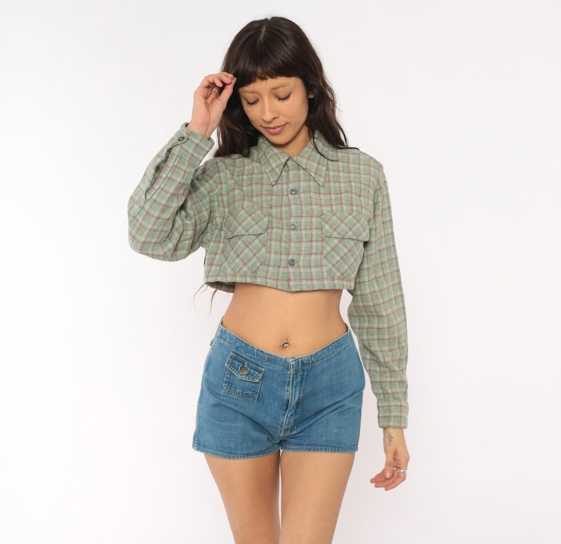 Puede incluir: Una camisa corta de manga larga con botones en un patr&oacute;n de cuadros verde salvia y rojo con dos bolsillos en el pecho, combinada con pantalones cortos de mezclilla azul con un peque&ntilde;o bolsillo frontal. La camisa tiene cuello puntiagudo.