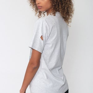 May include: A gray t-shirt with a distressed look. The shirt has a small hole in the left sleeve.