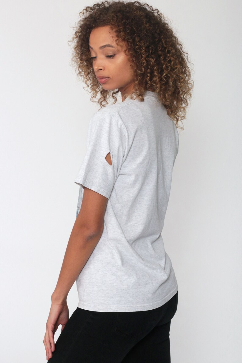 May include: A gray t-shirt with a distressed look. The shirt has a small hole in the left sleeve.