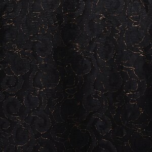 Puede incluir: Primer plano de una tela de encaje negro con un dise&ntilde;o floral. El encaje presenta hilo met&aacute;lico dorado que perfila el dise&ntilde;o floral. La tela tiene una apariencia delicada y texturizada, adecuada para prendas o proyectos de artesan&iacute;a.