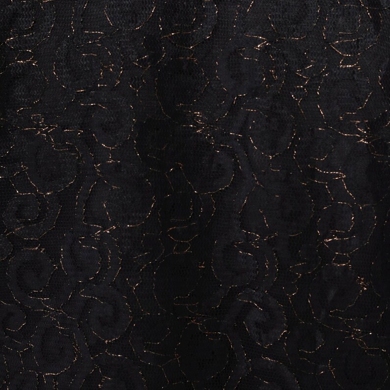Puede incluir: Primer plano de una tela de encaje negro con un dise&ntilde;o floral. El encaje presenta hilo met&aacute;lico dorado que perfila el dise&ntilde;o floral. La tela tiene una apariencia delicada y texturizada, adecuada para prendas o proyectos de artesan&iacute;a.