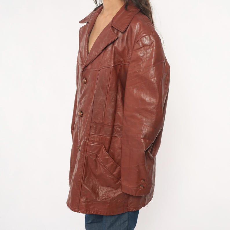 May include: A brown leather jacket with a collared neckline, button closure, and front pockets. The jacket has a classic design and a slightly worn appearance. The leather appears to be a reddish-brown color.