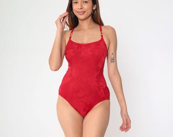 Pode incluir: Maiô vermelho de uma peça com um padrão floral texturizado e ferragens douradas. O maiô tem um decote redondo e alças finas.