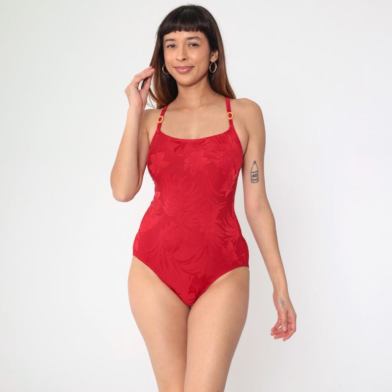 Peut inclure: Maillot de bain rouge une pi&egrave;ce avec un motif floral textur&eacute; et des accessoires dor&eacute;s. Le maillot de bain a un d&eacute;collet&eacute; arrondi et des bretelles fines.