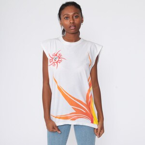May include: White sleeveless t-shirt with an orange and yellow sun design and the text "Malibu" on the front.