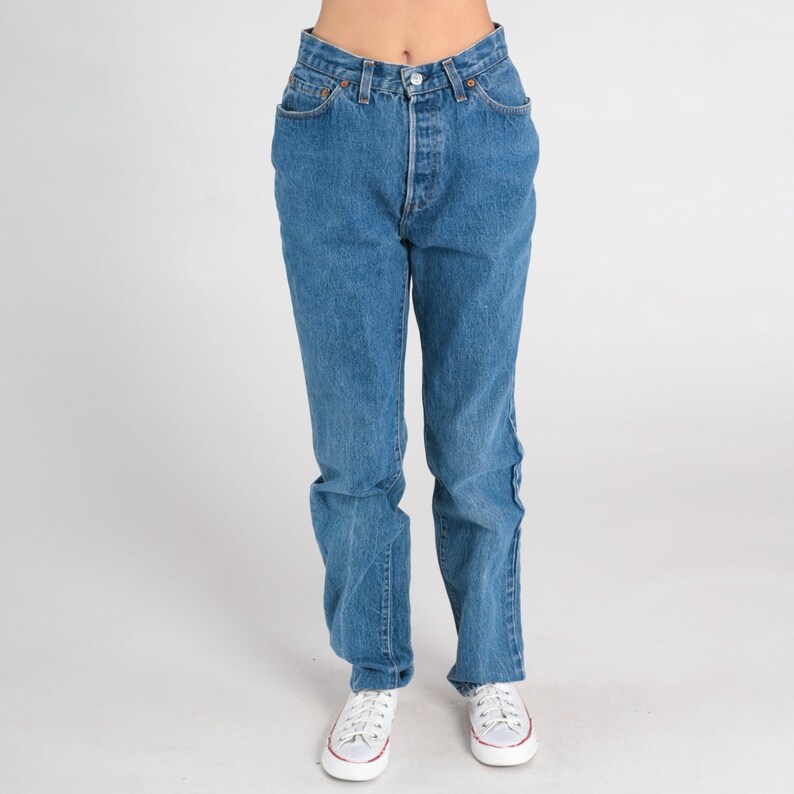 May include: A pair of blue denim jeans with a button fly and five pockets. The jeans are straight-legged and have a classic fit.