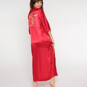 May include: A vibrant red satin robe with a dragon embroidery on the back. The robe has wide sleeves and a floor-length design. The dragon embroidery features gold, orange, and green thread. The robe is a solid, bright red color.