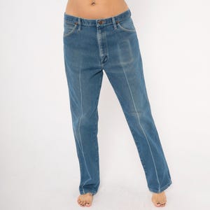 Peut inclure: Jean bleu clair avec une coupe droite. Le jean a une conception classique &agrave; cinq poches, une fermeture &agrave; bouton et &agrave; glissi&egrave;re, et des coutures blanches sur le devant des jambes. Le jean est de couleur moyenne et semble vintage.