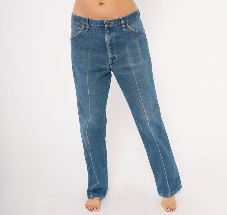 Peut inclure: Jean bleu clair avec une coupe droite. Le jean a une conception classique &agrave; cinq poches, une fermeture &agrave; bouton et &agrave; glissi&egrave;re, et des coutures blanches sur le devant des jambes. Le jean est de couleur moyenne et semble vintage.