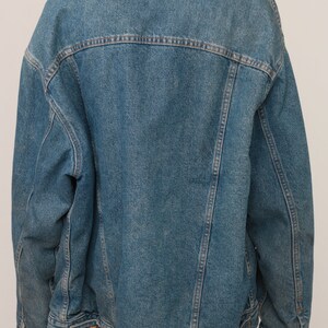 Puede incluir: Una chaqueta de mezclilla azul con un cuello de sherpa de color crema. La chaqueta tiene mangas largas, un canes&uacute; en la espalda y detalles de costuras verticales. La tela de mezclilla tiene un lavado azul medio con costuras visibles.