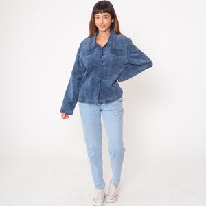 May include: A blue corduroy jacket with button closures and two chest pockets. The jacket is paired with light blue jeans and white sneakers. The outfit is worn by a person with brown hair.