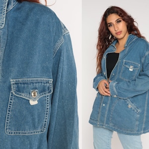 May include: A medium-wash denim jacket with a button-up front, two chest pockets, and a collared neckline. The jacket has silver-tone buttons and pocket details. The sleeves are long and the jacket appears to be oversized.