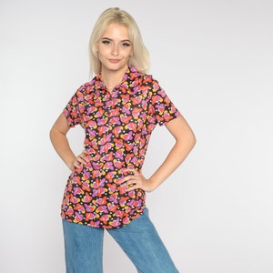 May include: A black short-sleeved shirt with a colorful pattern of pink, orange, and yellow hearts. The shirt has a collared neckline and a button-up front.