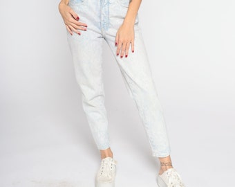 May include: A pair of light blue acid wash jeans with a high waist and a straight leg fit. The jeans are being worn by a person with white trainers.