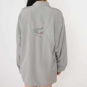 May include: A gray long-sleeved shirt with a white embroidered crocodile logo on the back.