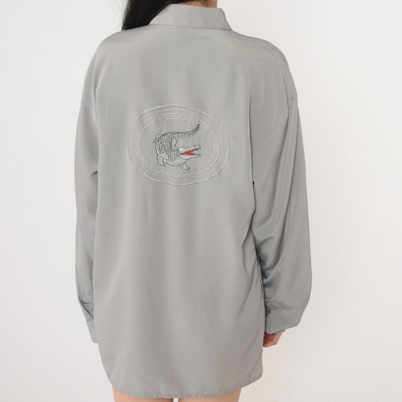 May include: A gray long-sleeved shirt with a white embroidered crocodile logo on the back.