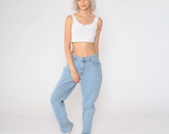 May include: A woman wearing a white crop top and light blue, high-waisted, baggy jeans. She is standing with her feet slightly apart and her hands on her hips.