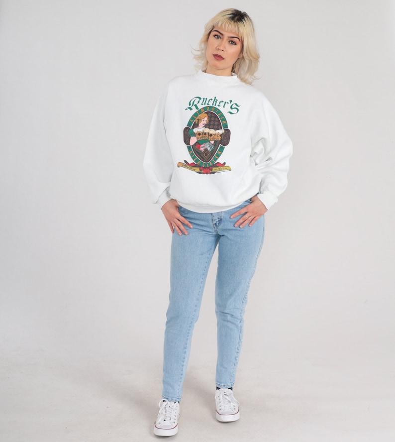 May include: White sweatshirt with a green and white logo that says "Rucker's" and features a woman holding a beer stein. The logo is surrounded by a green oval.