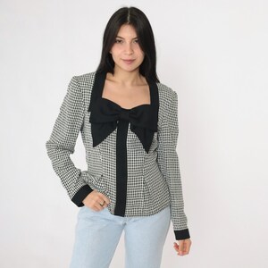 May include: A black and white gingham blazer with a large black bow at the neckline. The blazer has long sleeves and a fitted silhouette.