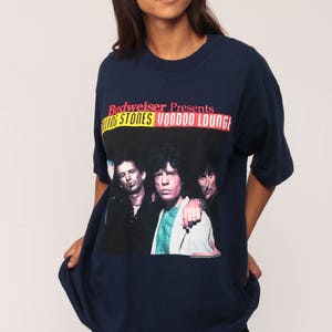 May include: Navy blue t-shirt featuring a graphic of The Rolling Stones with the text "Budweiser Presents Rolling Stones Voodoo Lounge". The shirt has a crew neck and short sleeves.