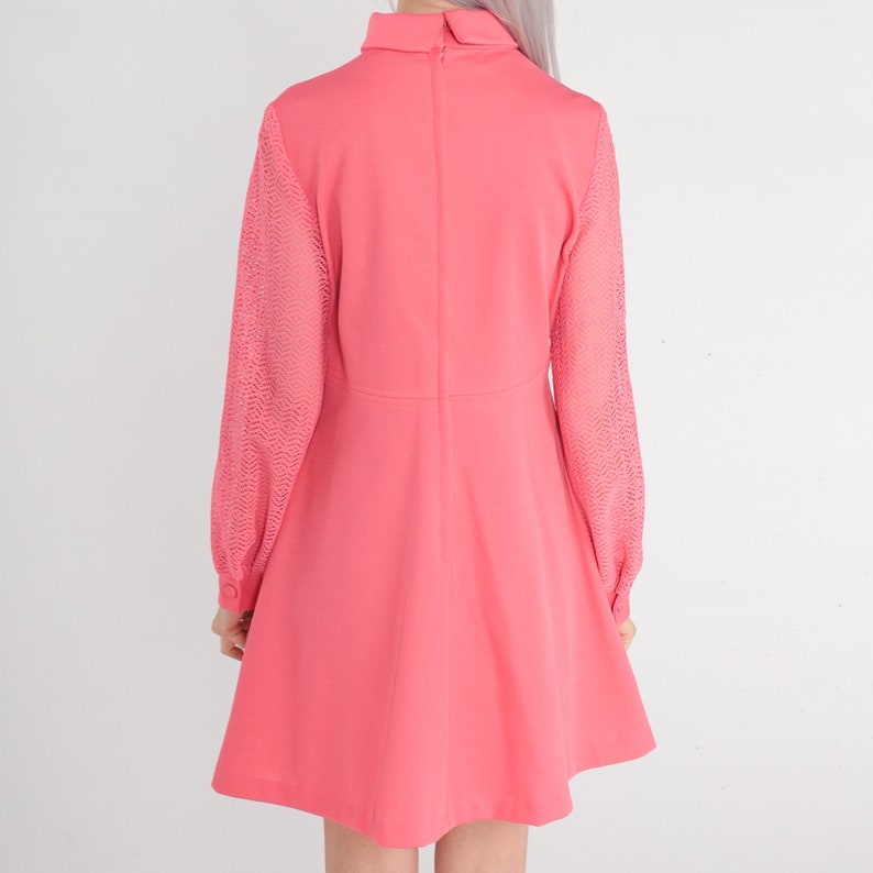 May include: A pink dress with long sleeves. The sleeves are made of a sheer lace fabric. The dress has a high neckline and a slightly flared skirt.