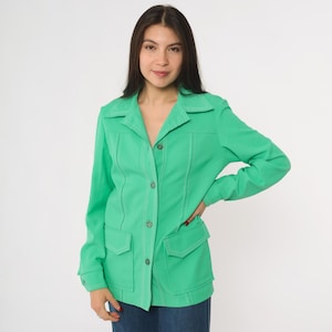 May include: A vibrant green jacket featuring a collared design, two front pockets, and contrasting stitching. The jacket has long sleeves and is fastened with buttons. The jacket is worn with blue jeans.