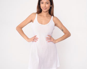May include: White slip dress with spaghetti straps. The dress has a scoop neckline and a flared skirt. The fabric appears to be a mesh or open-weave material. The dress is knee-length and has a simple, classic design.