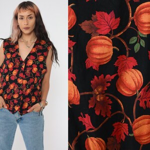 Puede incluir: Un chaleco negro sin mangas con un estampado de oto&ntilde;o de calabazas naranjas y hojas rojas. El chaleco tiene cuello en V y cierre de bot&oacute;n.