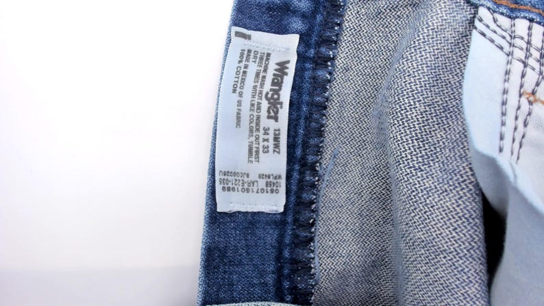 Puede incluir: Primer plano de unos vaqueros de mezclilla azules con una etiqueta Wrangler. La etiqueta indica la talla 34 x 33. Los vaqueros son 100% algod&oacute;n y est&aacute;n fabricados en M&eacute;xico con tejido estadounidense.