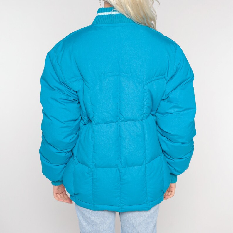 May include: A bright turquoise puffer jacket with a white ribbed collar and cuffs.