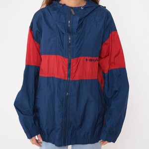 May include: A blue and red windbreaker jacket with a zipper closure and a hood. The jacket has the word "HEAD" printed on the front.