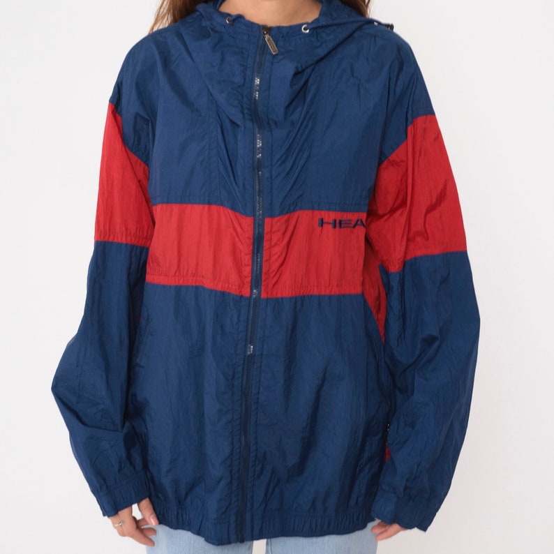 May include: A blue and red windbreaker jacket with a zipper closure and a hood. The jacket has the word "HEAD" printed on the front.