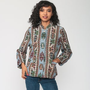 May include: A light blue jacket with a colorful geometric pattern. The jacket has long sleeves, a button-up front, and two pockets. The pattern includes red, green, and brown shapes. The jacket is worn with blue jeans.