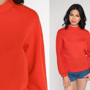 May include: A bright orange mock neck sweatshirt with long sleeves and a slightly puffed sleeve design.