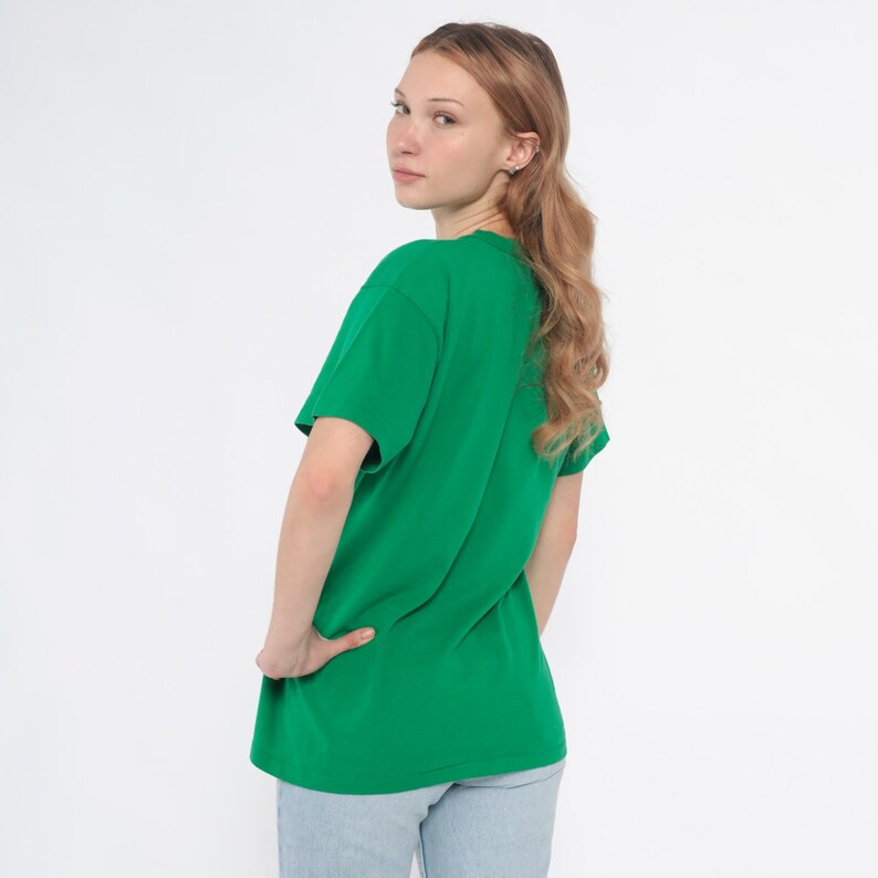 K&ouml;nnte beinhalten: Ein einfarbiges gr&uuml;nes T-Shirt. Das kurz&auml;rmelige Shirt hat einen leuchtenden Gr&uuml;nton. Das Model tr&auml;gt hellblaue Jeans. Der Hintergrund ist schlicht wei&szlig;.