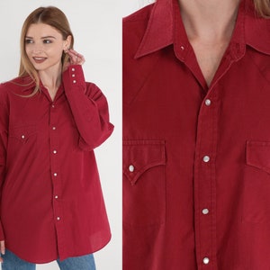 May include: A red long-sleeved button-down shirt with a pointed collar and two chest pockets. The shirt has a classic Western style.