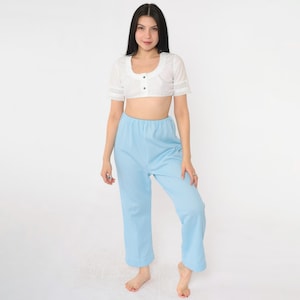 Puede incluir: Una blusa blanca recortada con ribete de encaje y un cierre de botón único, combinada con pantalones a cuadros azul claro.