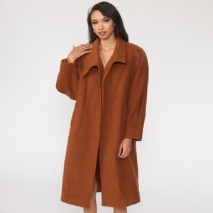 May include: A long brown coat with a wide collar and a single button closure. The coat is made of a soft, textured fabric.